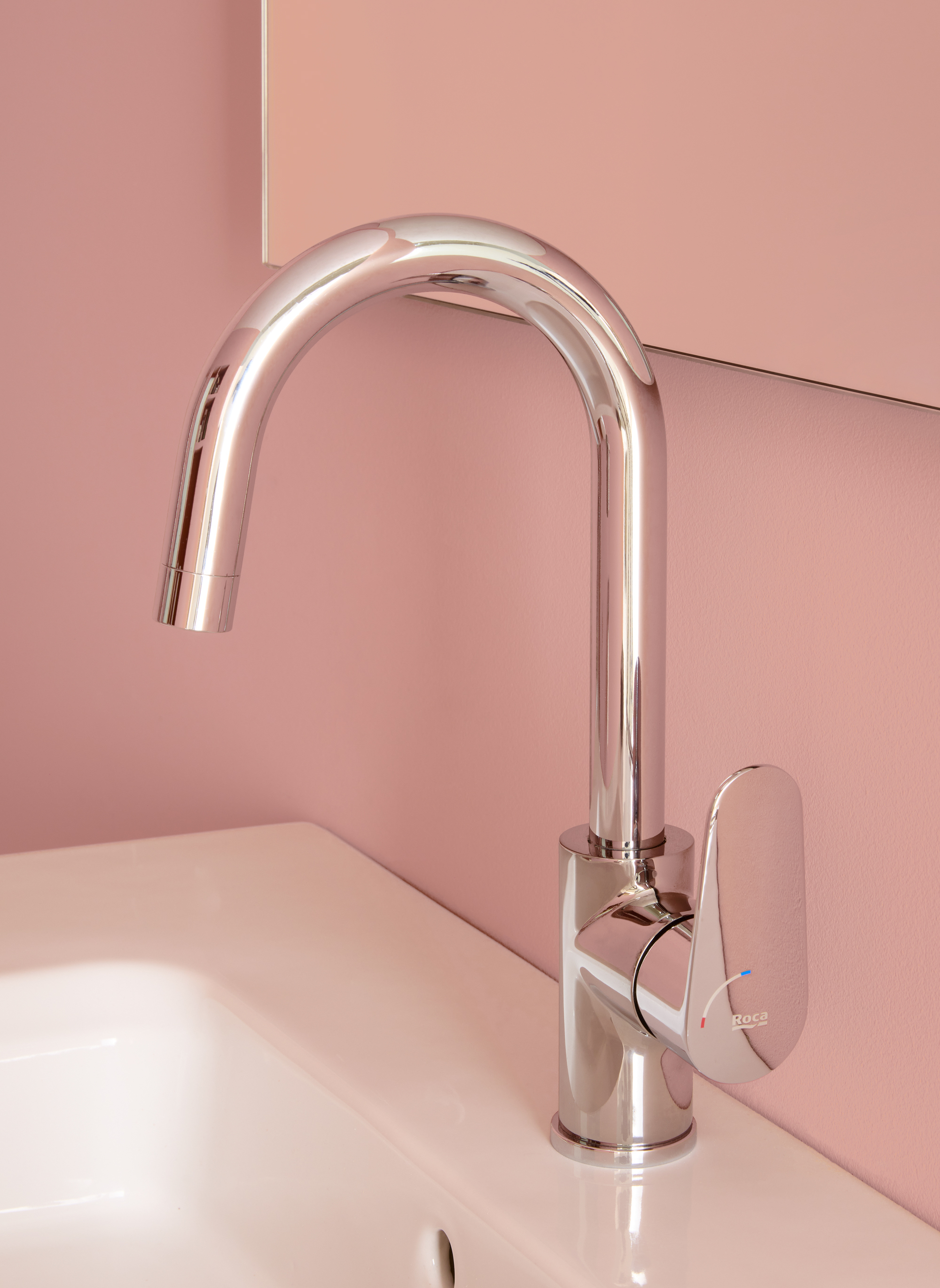 Chrome curved high-arc faucet over a white sink, mounted on a pink wall; sleek lever handle with blue and red indicators.