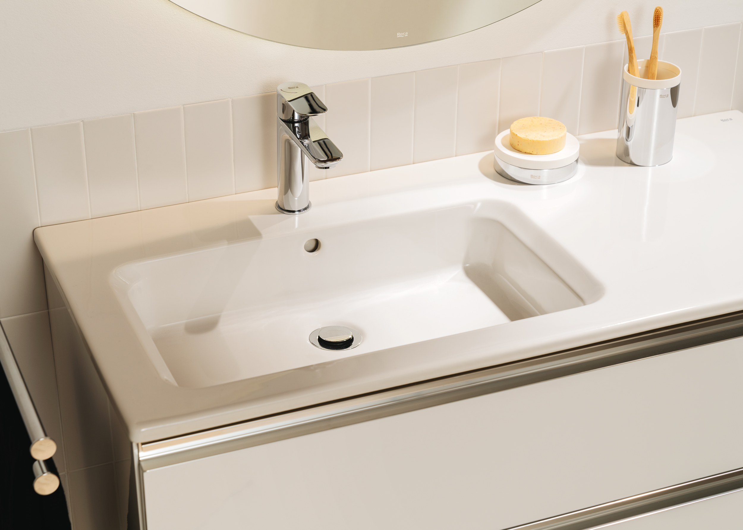 White bathroom sink with chrome faucet, soap on a dish, and a toothbrush holder with two wooden toothbrushes on a glossy white counter.