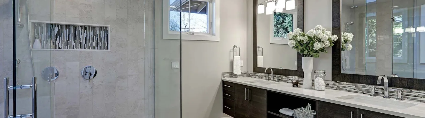 Modern bathroom with a glass-enclosed shower, double vanity, dark wood cabinetry, large framed mirrors, white countertops, and a vase of white flowers.