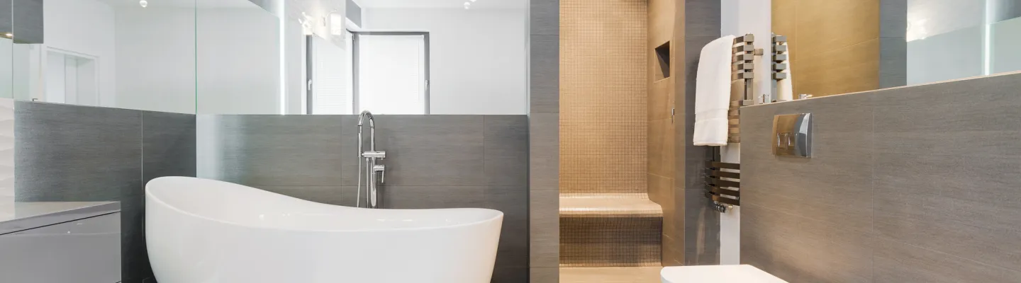 Modern grey-tiled bathroom with a freestanding white bathtub, wall-hung toilet and bidet, glass shower alcove, heated towel rail and mirrored walls.