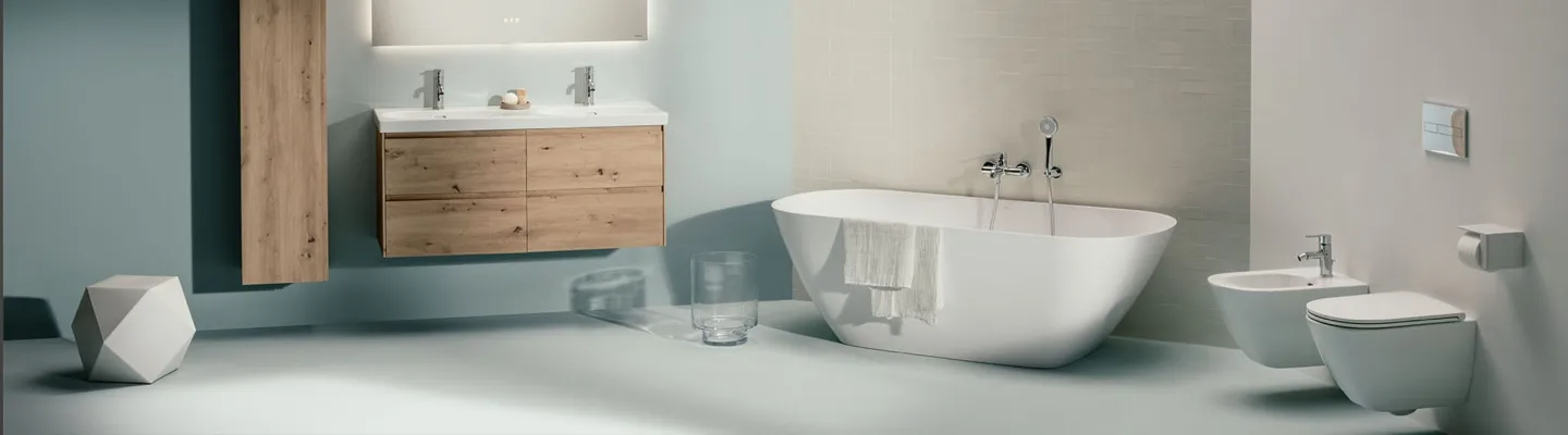 Modern bathroom with a white freestanding tub, a wooden double vanity with two sinks, a bidet and toilet, pale blue walls and light grey floor.