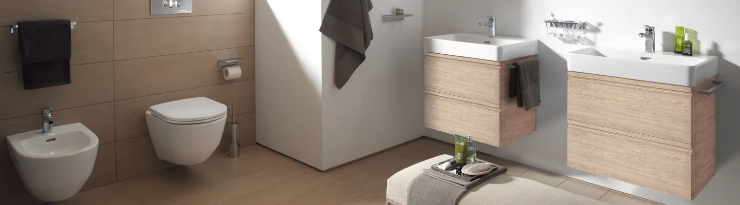 Modern bathroom with beige wood-tiled walls, wall-hung toilet and bidet, and floating vanities with white basins; towels and toiletries on display.