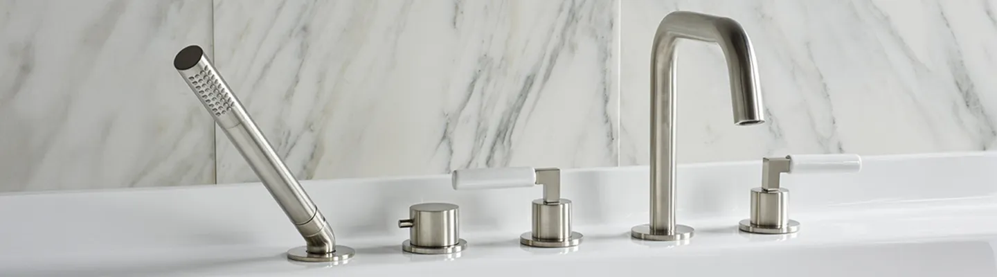 Brushed stainless steel bathroom faucet set with a handheld shower head, two knob handles, and a curved gooseneck spout against a marble tiled wall.
