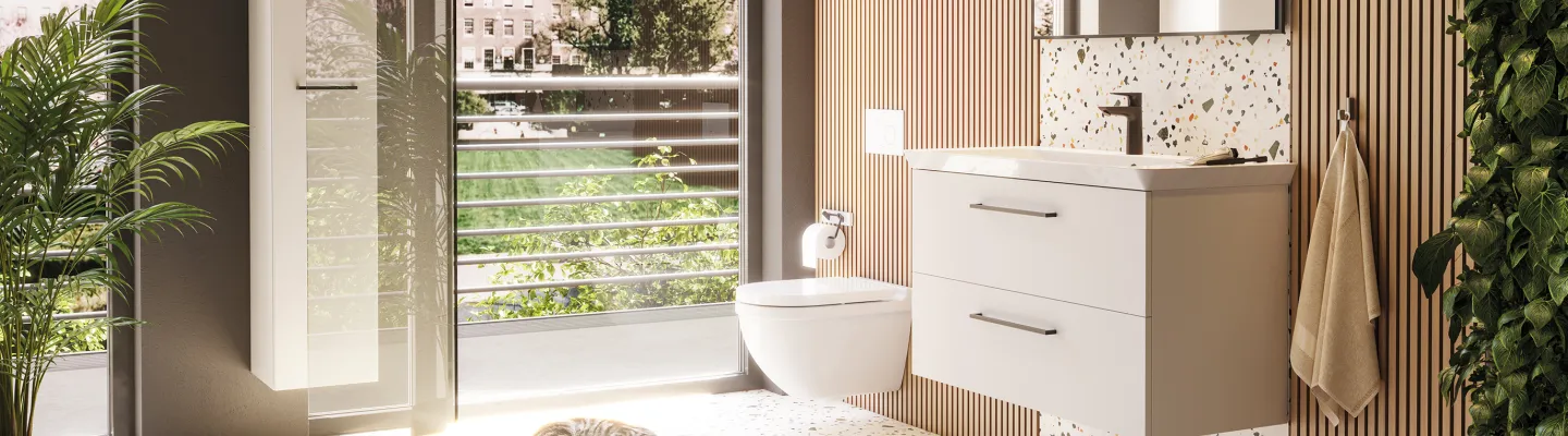 Bright modern bathroom with terrazzo floor, wall-mounted vanity, glass door to balcony, and sleeping cat in sunshine; lush plants and wood slats.