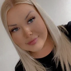 Close-up of a person with long blonde hair, blue eyes and light makeup, wearing a black top, with a soft smile against a neutral background. profile photo