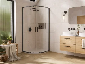 Bright modern bathroom with a curved glass shower enclosure, a wooden double vanity, large mirror, wall sconce, and a frosted window.