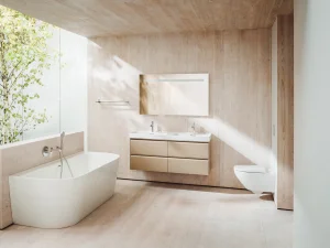Bright bathroom with light wood panels, a white freestanding tub, beige floating vanity with double sinks, and a glass wall with a tree outside.