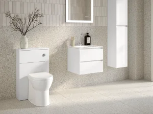 Minimalist white bathroom with wall-mounted vanity and sink, floating storage drawers, terrazzo walls and floor, a backlit mirror, vase with branches and a window.