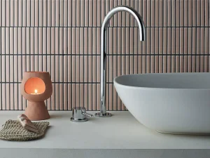 Modern bathroom with oval white basin and chrome curved faucet, terracotta candle holder with a lit candle, woven mat and seashell on countertop.