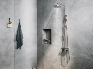 Concrete grey bathroom with a tall rain shower on the right, a handheld unit and hose; a recessed niche holds a candle and diffuser; a towel and small bag hang on the left.