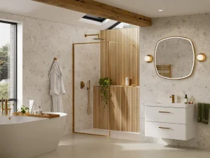 Bright contemporary bathroom with a freestanding white tub, glass shower with wooden slats, skylight, white vanity, oval backlit mirror and gold fixtures.