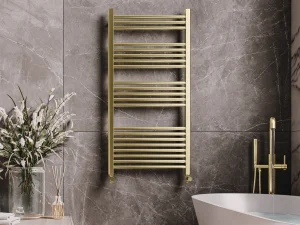 Luxurious bathroom with a gold towel radiator on grey marble walls, a white freestanding tub with gold fixtures, and a vase of white flowers on a wooden surface.