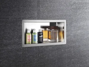Recessed stainless shelf in dark tile wall with two green L’Occitane bottles, a Biotherm Homme bottle, and a Dolce & Gabbana perfume.