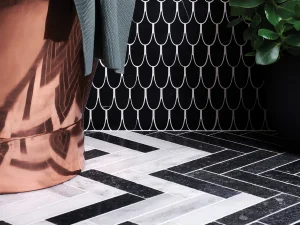 Corner of a room with a black wall featuring a white scallop pattern, copper drape on the left, grey fabric, a potted plant, and a black-and-white chevron floor.