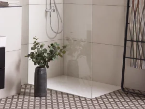 Modern bathroom with a glass shower enclosure, chrome rainfall and handheld shower, beige tiles, a patterned towel rack, and a vase of eucalyptus.