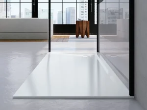 Modern interior with glass walls and city skyline view; white rectangular shower tray in the foreground, grey seating to the left, and a wooden stool.
