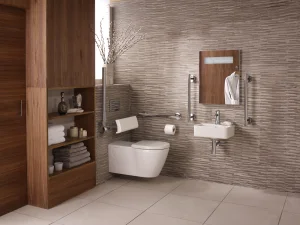 Modern accessible bathroom with wall-mounted toilet and sink, wooden storage shelves, beige mosaic wall tiles, mirror, grab bars and towels.