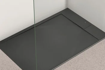 Corner shower with a dark grey rectangular tray, a transparent glass panel on the left, white walls and a light speckled floor.