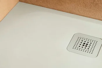 Light grey shower floor with a square, perforated drain in the corner, framed by brown textured walls.