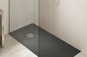 Minimalist bathroom shower area with a dark slate tray, clear glass partition, light tiled walls, and a handheld showerhead.