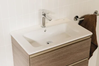 Wall-mounted bathroom vanity with a white rectangular sink, chrome faucet, and a two-drawer wood cabinet; a brown towel hangs on a chrome rail.