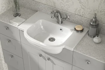 White ceramic sink in a grey cabinet vanity with a speckled countertop; chrome taps, soap dish, pump, reed diffuser, and white flowers.