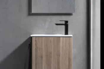 Minimalist bathroom vanity with a light wood cabinet, white sink and black faucet on a grey concrete wall; open shelf holds bottles and a soap dish.