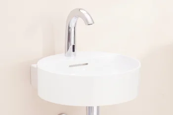 White round wall-mounted sink with a chrome curved faucet and exposed chrome pipe against a pale beige wall.