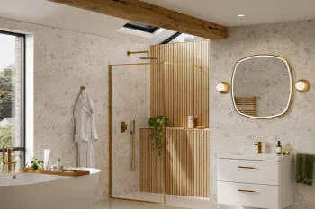 Bright contemporary bathroom with a freestanding white tub, glass shower with wooden slats, skylight, white vanity, oval backlit mirror and gold fixtures.