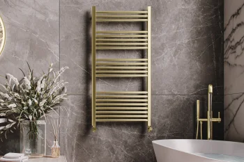 Luxurious bathroom with a gold towel radiator on grey marble walls, a white freestanding tub with gold fixtures, and a vase of white flowers on a wooden surface.