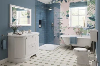 Bright bathroom with a white vanity and framed mirror, glass-walled blue-tiled shower, freestanding clawfoot tub, pink floral wallpaper and a window.