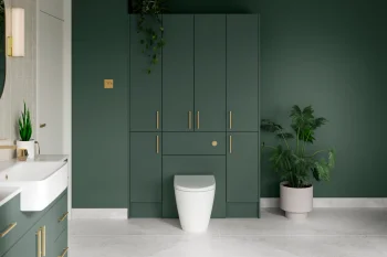 Modern bathroom with tall dark green cabinetry and gold handles, a central white toilet, white sink to the left, grey tile floor, and hanging and potted greenery.