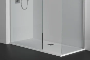 A modern shower enclosure with clear glass panels and chrome fixtures; handheld shower on the left, recessed shelf with bottles on the right, and a white tray.