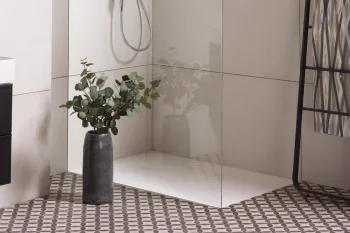 Modern bathroom with a glass shower enclosure, chrome rainfall and handheld shower, beige tiles, a patterned towel rack, and a vase of eucalyptus.
