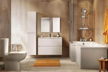 Contemporary bathroom with beige tiles and white fixtures: toilet, tall cabinet, floating vanity with mirror, glass shower over a tub, and an orange towel with mat.