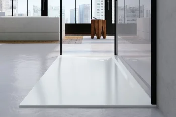 Modern interior with glass walls and city skyline view; white rectangular shower tray in the foreground, grey seating to the left, and a wooden stool.