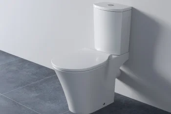 White modern two-piece toilet with closed lid against a pale wall, on a dark grey tiled bathroom floor.