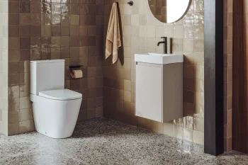 Modern bathroom with beige glossy tiled walls, circular mirror above a white wall-mounted vanity, black faucet, beige towel, and a white toilet.