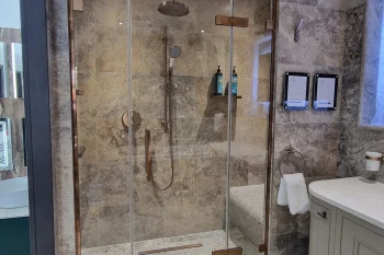 Luxurious marble bathroom featuring a glass shower enclosure with brass hardware, rainfall and handheld showers, a tiled bench, and a curved grey vanity.