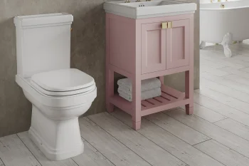 White toilet beside a pink vanity with a white sink and gold fixtures in a stylish bathroom; a clawfoot tub and round mirror in the background.