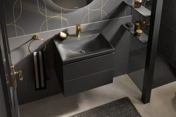 Dark grey bathroom featuring a matte black vanity with a gold faucet, round mirror, gold towel ring, geometric wallpaper, glass shower and shelves.