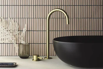 Modern bathroom vanity with a matte black round vessel sink, gold curved tap, gold knob, glass vase with dried ferns, beige tiled wall.