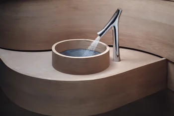 Minimalist wooden bathroom with a round wooden basin and a tall chrome faucet pouring water into it.