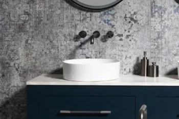 Blue bathroom vanity with a white circular vessel sink on a marble counter, wall-mounted taps, and small bottles; distressed grey wall with round mirrors.