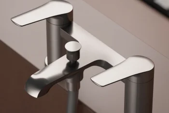 Close-up of a sleek chrome bath mixer with two flat lever handles, a curved spout, and a hose, mounted on a tan bathroom edge.