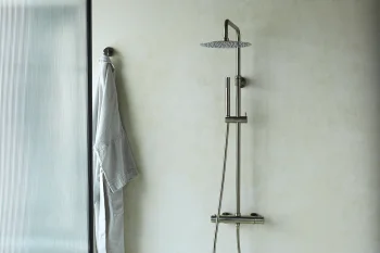 Minimalist shower area with a tall chrome rain head, a vertical rail-mounted handheld unit, and a grey towel hanging beside a frosted glass panel.