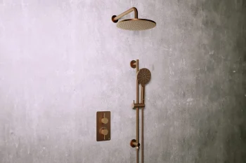 Bronze shower system mounted on a textured grey wall, featuring a large rain showerhead, a vertical bar with handheld nozzle, and dual controls.
