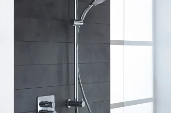 Modern chrome shower system with a square rain head, handheld shower on a vertical rail, glass partition and a dark tiled wall.