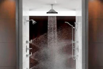 A modern white shower enclosure with a ceiling rainfall head and multiple side jets, water spraying inside the glass-walled cabin.