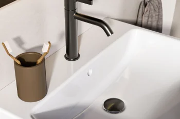 Matte black bathroom faucet with a gold cap over a white sink; a brown toothbrush holder with two toothbrushes and a towel ring with a grey towel on the wall.